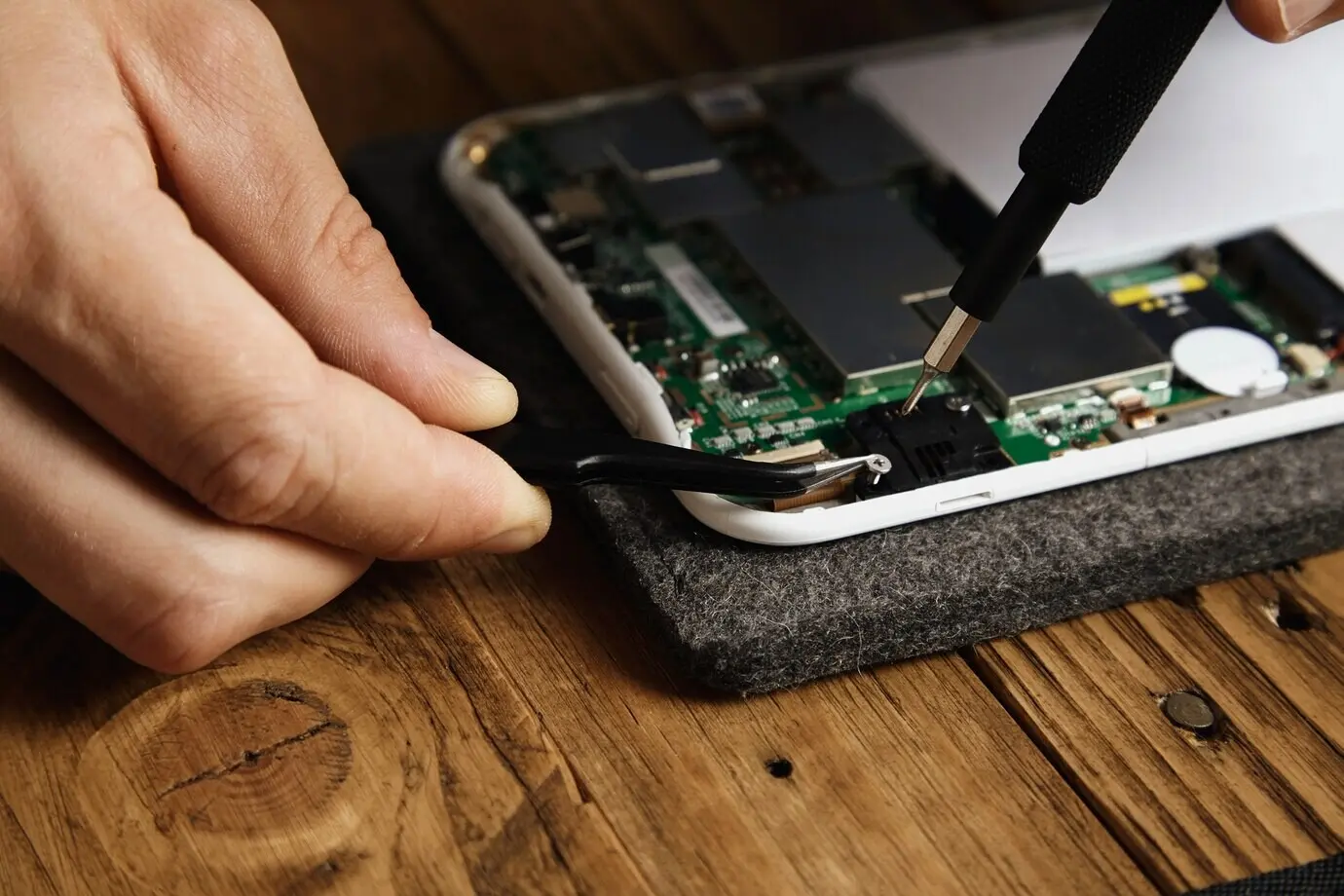 Ein Meister verwendet spezielle Werkzeuge, um ein elektronisches Gerät sorgfältig zu zerlegen: Zange und Bit-Schraubendreher.